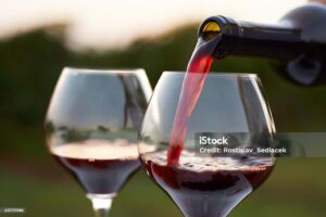 Pouring red wine into glasses in the vineyard at sunset