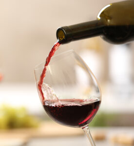 Pouring,Red,Wine,From,Bottle,Into,Glass,On,Blurred,Background