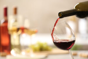 Pouring,Red,Wine,From,Bottle,Into,Glass,On,Blurred,Background