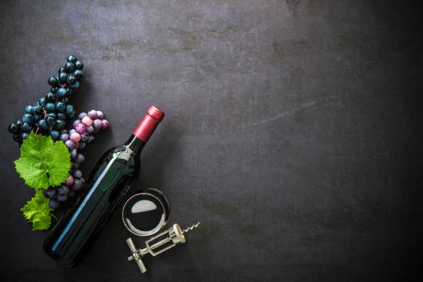 Bottle of red wine, wineglass, grapes and corks on dark background